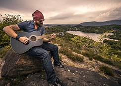 山の上にある小岩に腰掛けて、ギターを引く男性