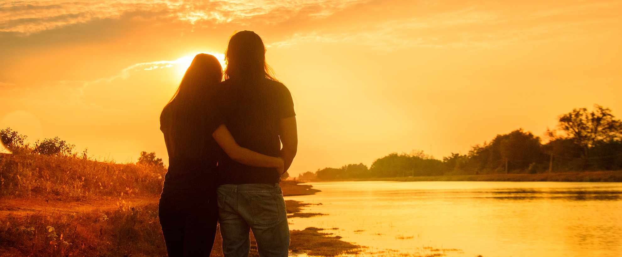 川の横で夕日を見ながら寄り添う男女